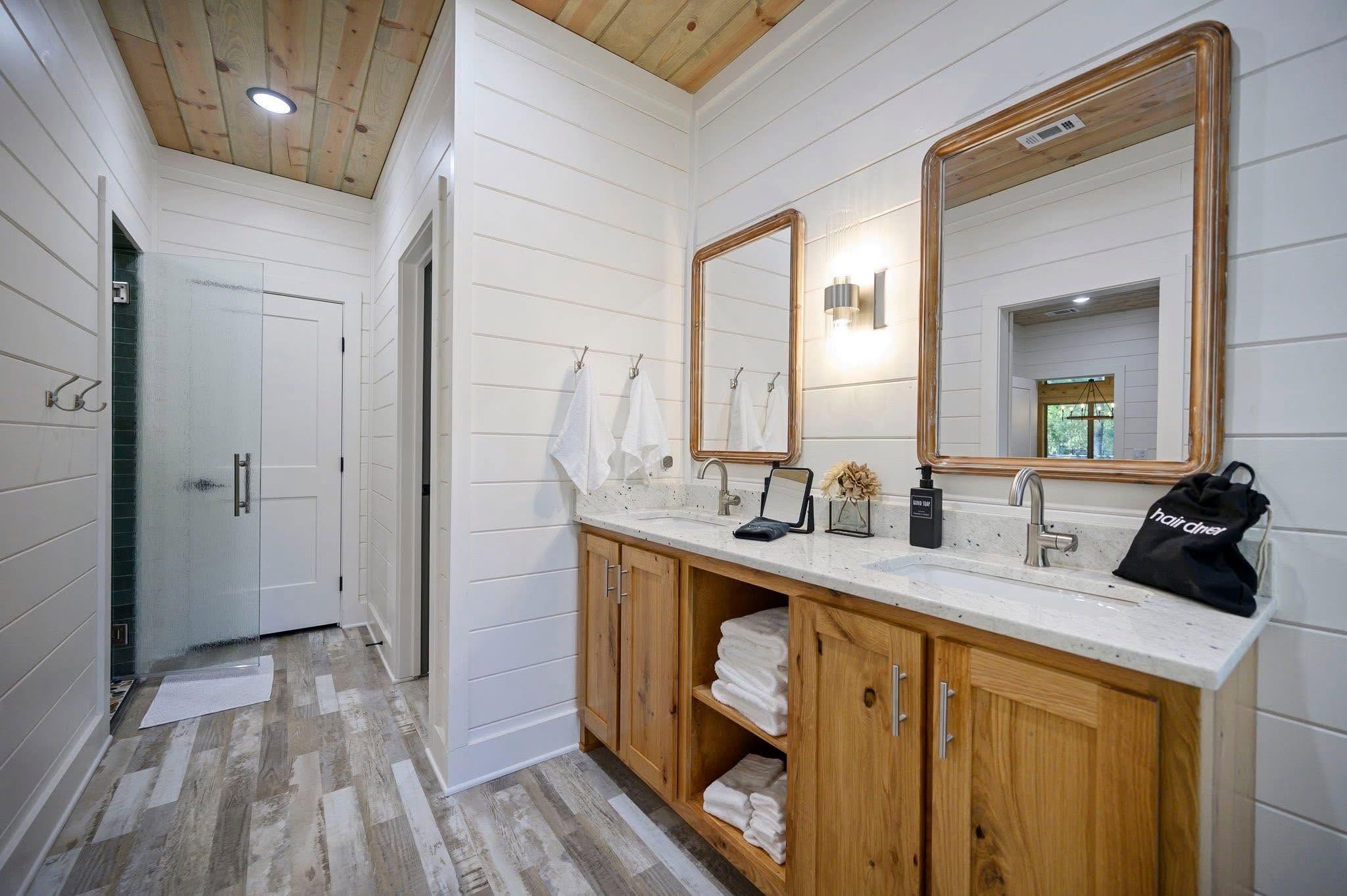 Modern bathroom interior with a wooden double vanity, dual mirrors, and light flooring.